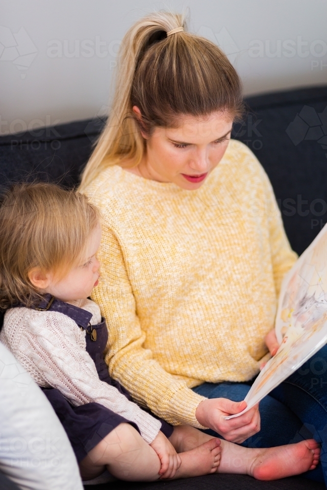 Mother reading a story book to her daughter at home - Australian Stock Image