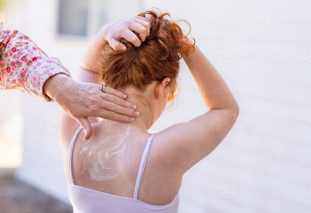 mother's hand rubbing sunscreen onto child's neck, while child holds her hair up - Australian Stock Image