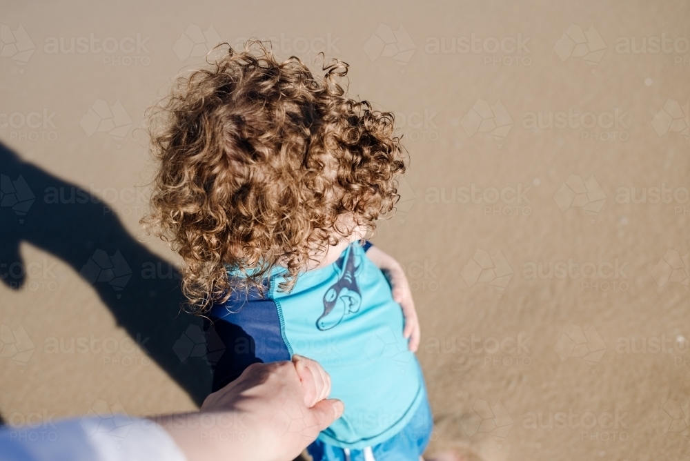 Mother's point of view looking down at her son while he holds her hand at the beach, Australia - Australian Stock Image