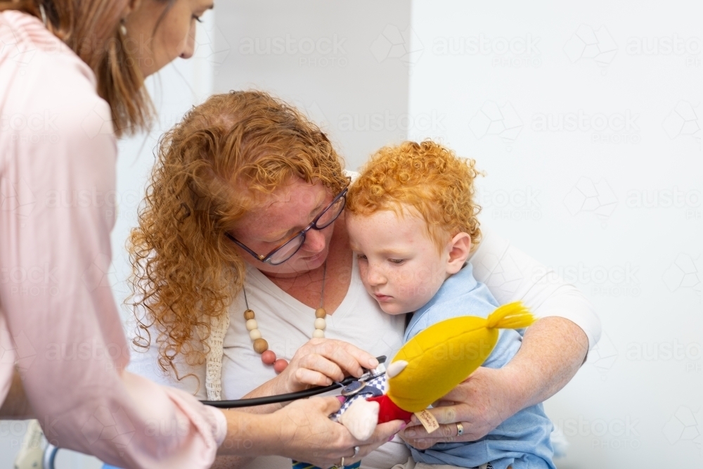 mother showing child how stethoscope works on toy - Australian Stock Image