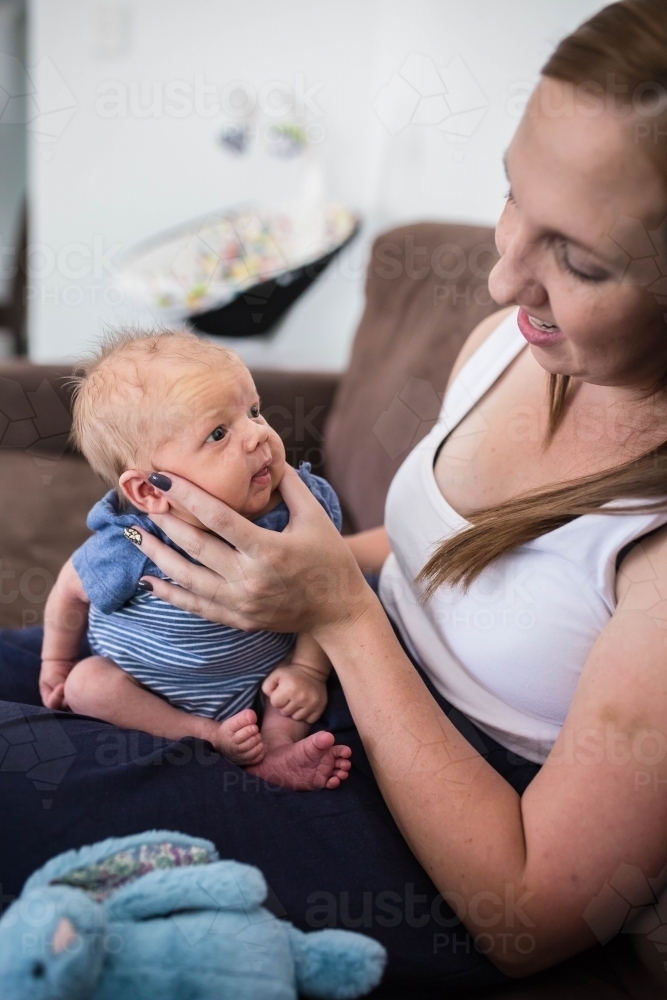 Mother sitting burping newborn baby boy holding his face smiling at each other - Australian Stock Image