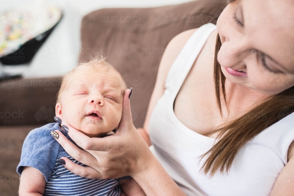 Mother smiling down at newborn baby boy while holding his face burping him - Australian Stock Image