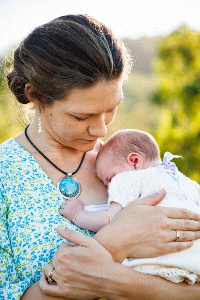Mother snuggling her new daughter outside in sunlight - Australian Stock Image