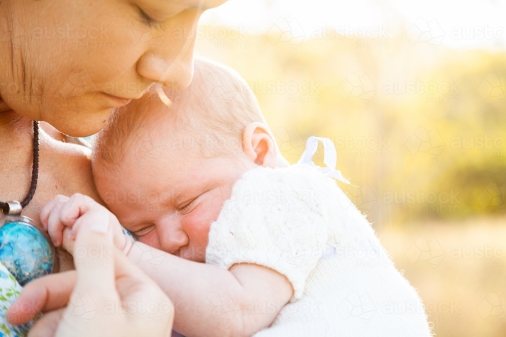 Mother snuggling with baby, holding hand in sunlight - Australian Stock Image