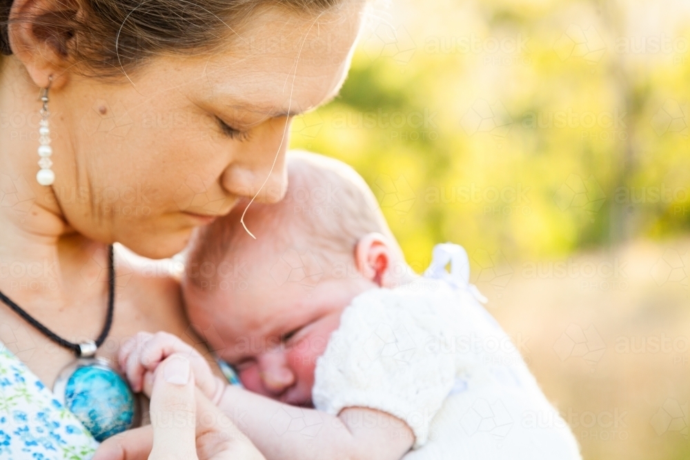Mother snuggling with baby, holding hand in sunlight - Australian Stock Image