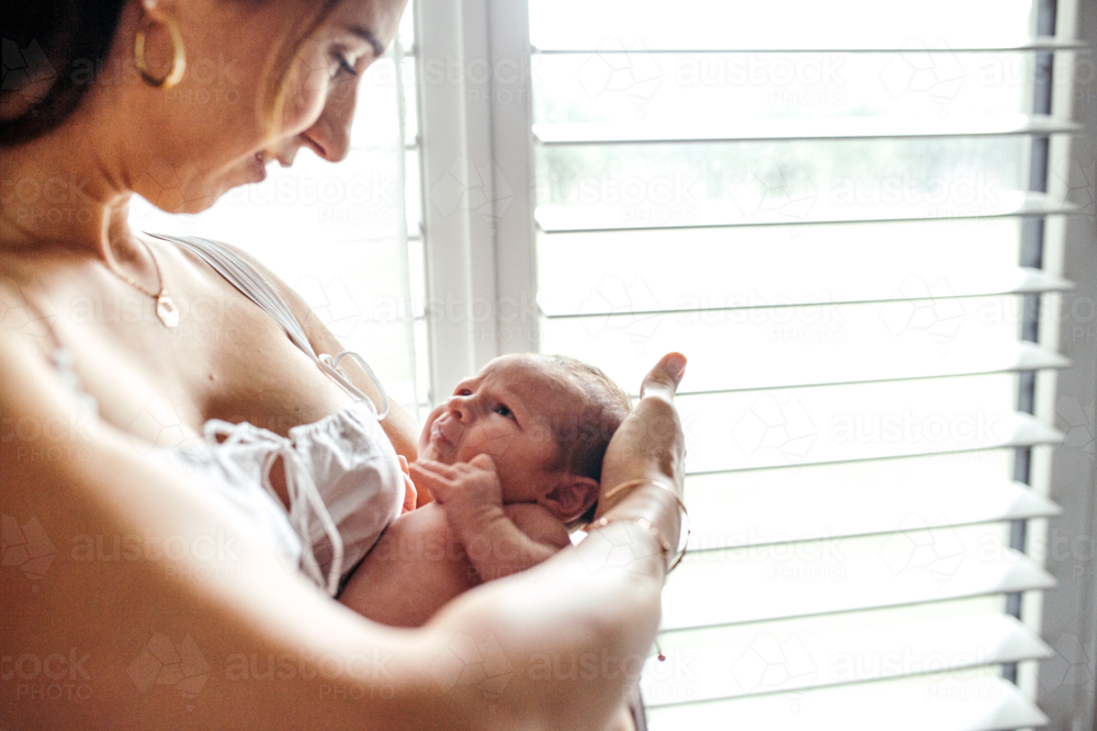 Mother standing beside the window touching Newborn baby's head - Australian Stock Image