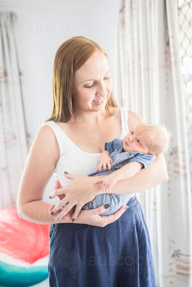 Mother standing nursing newborn baby boy smiling - Australian Stock Image