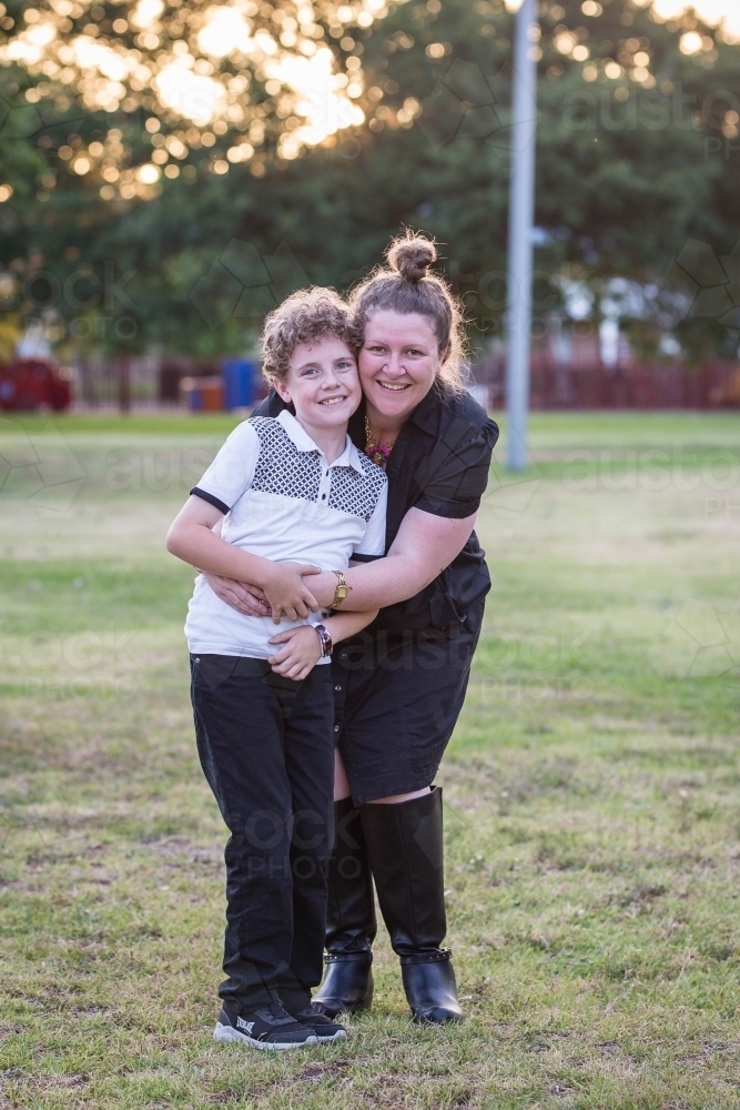 Mother standing with arms wrapped around son smiling - Australian Stock Image