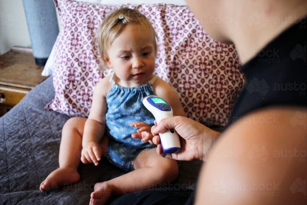Mother taking her baby daughter's temperature with a digital thermometer - Australian Stock Image