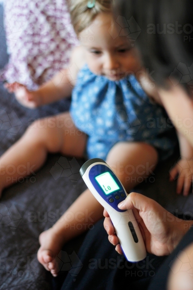 Mother taking her baby daughter's temperature with a thermometer - Australian Stock Image