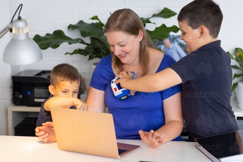 mother trying to work on laptop computer with kids interrupting her - Australian Stock Image