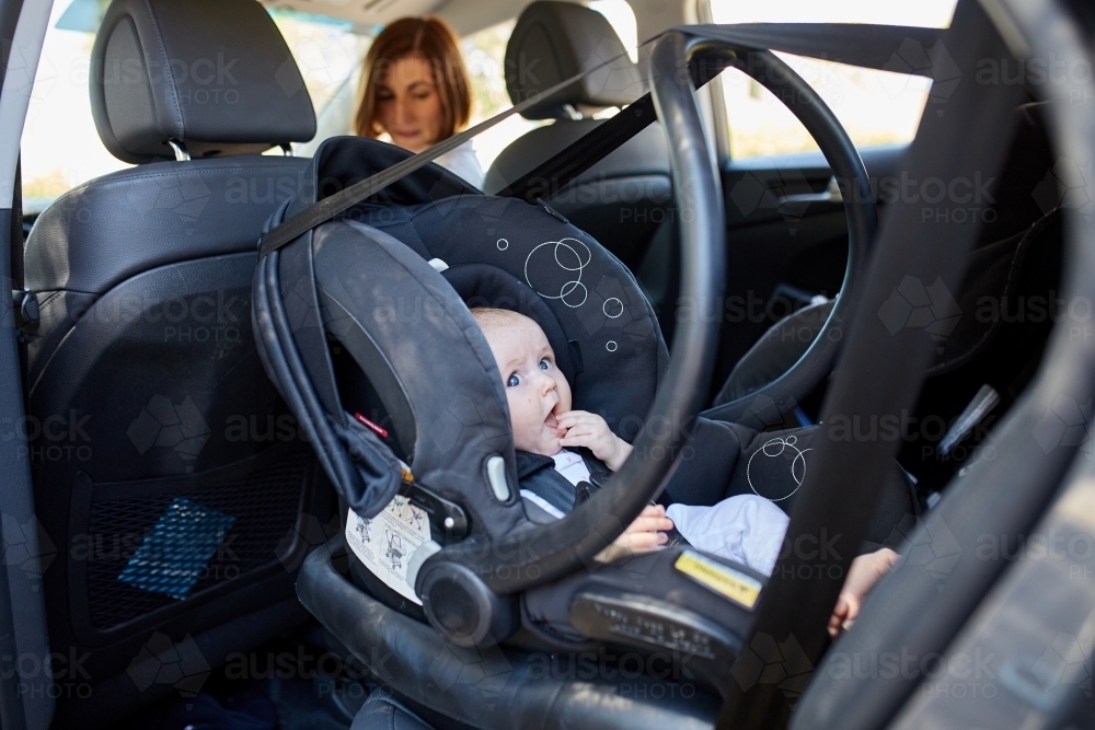 Mother turning to check baby in a rear-facing car seat - Australian Stock Image