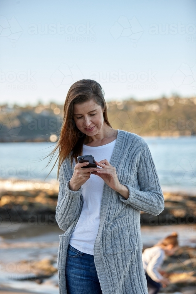Mother using phone at seaside - Australian Stock Image