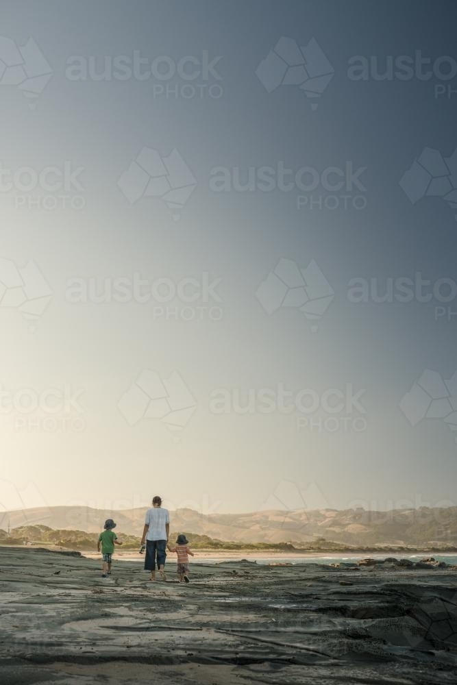 Mother walks with her mixed race boys looking for shells on a rocky coast - Australian Stock Image