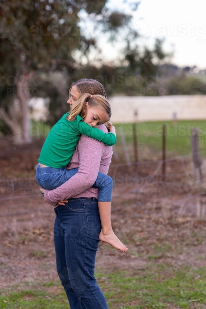 mother wearing jeans carrying her daughter on a country property - Australian Stock Image