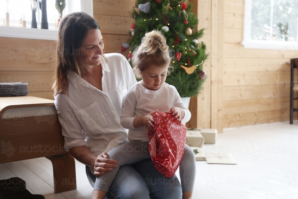 Mother with daughter opening present with Christmas tree in background - Australian Stock Image