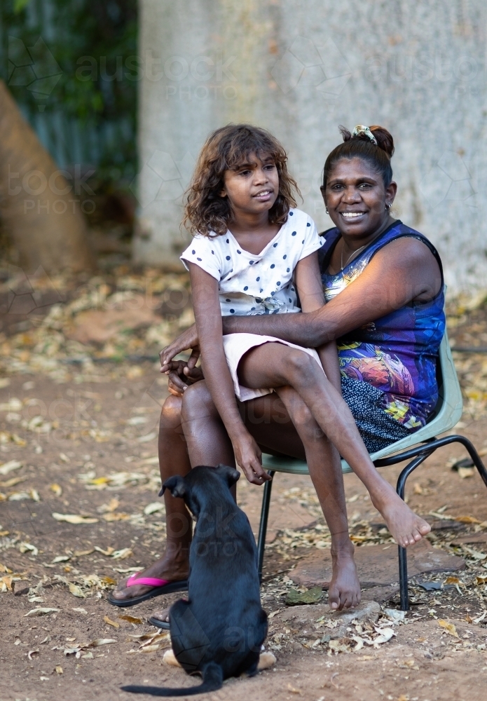 mother with daughter sitting on her lap in backyard - Australian Stock Image
