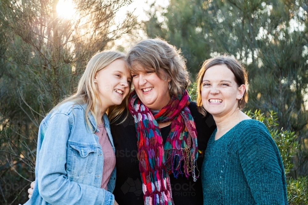 Mother with her two daughters hug together outside - Australian Stock Image