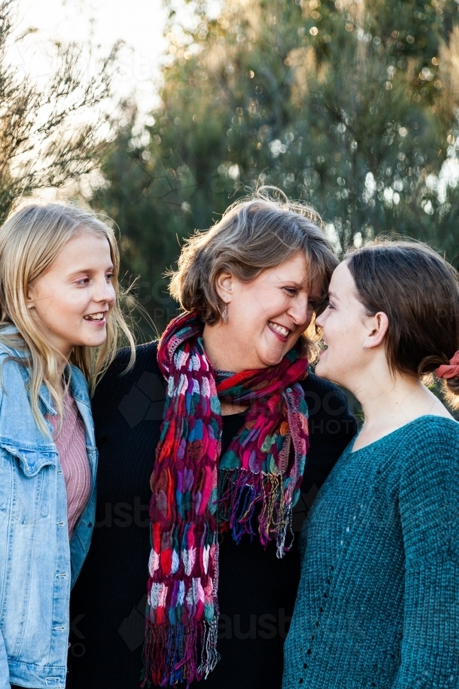 Mother with her two daughters hug together outside - Australian Stock Image