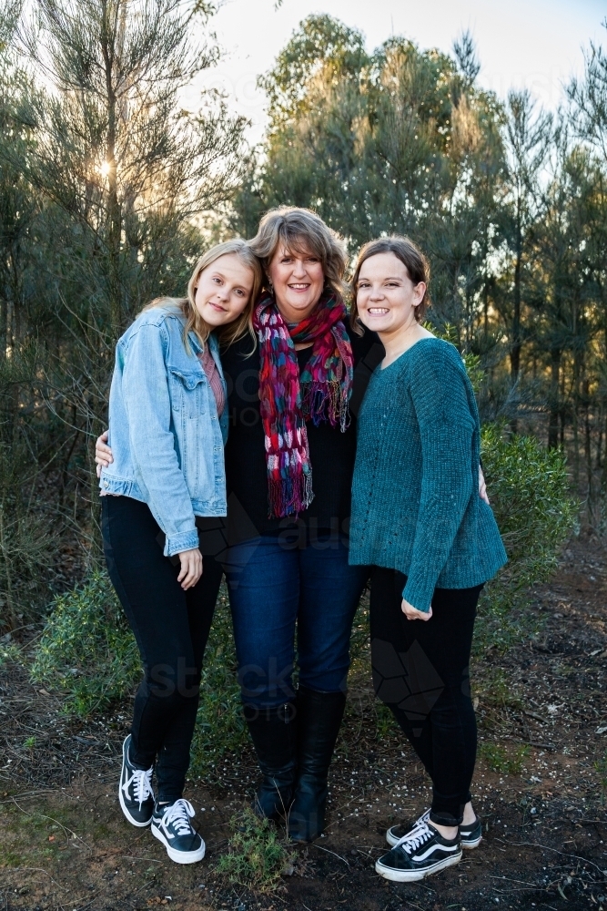Mother with her two daughters hug together outside - Australian Stock Image