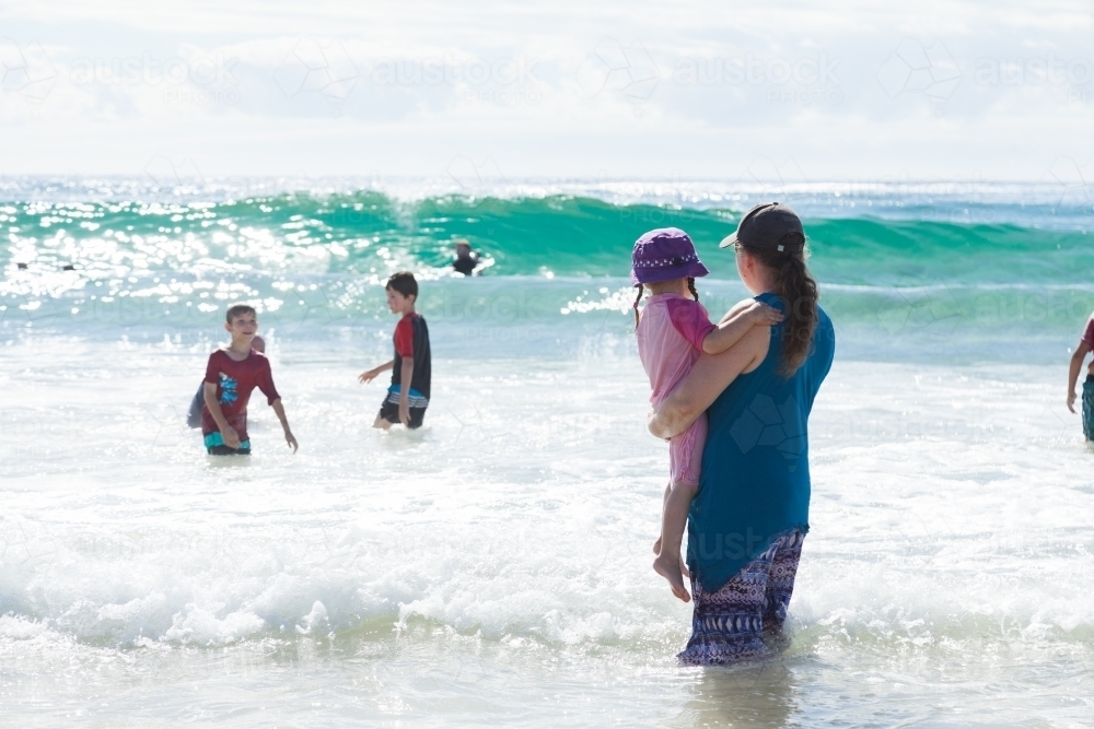 Mother with three kids playing in the waves at the seaside - Australian Stock Image