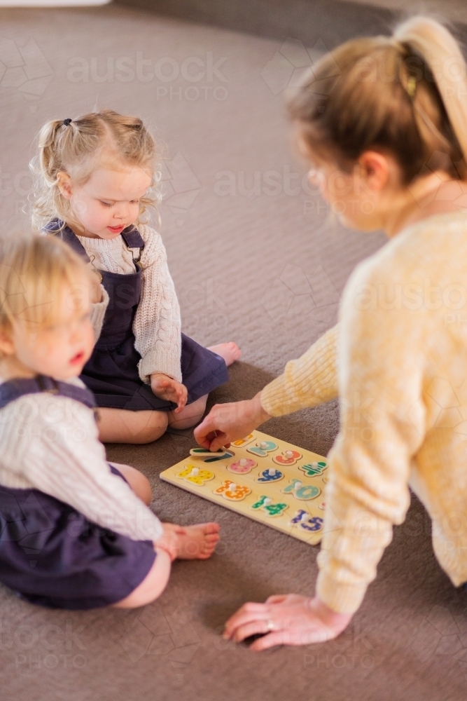 Mother with two young girls playing puzzles on lounge room floor - Australian Stock Image