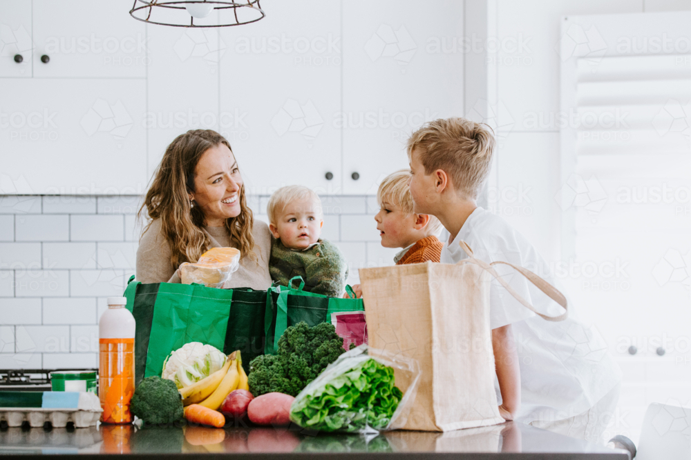 Mother with young boys unpacking groceries on the countertop in the kitchen - Australian Stock Image