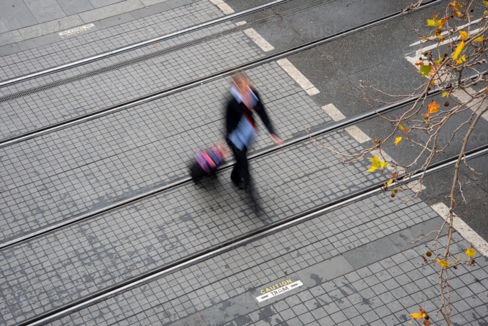 Motion blurred pedestrian crossing tram tracks seen from above - Australian Stock Image