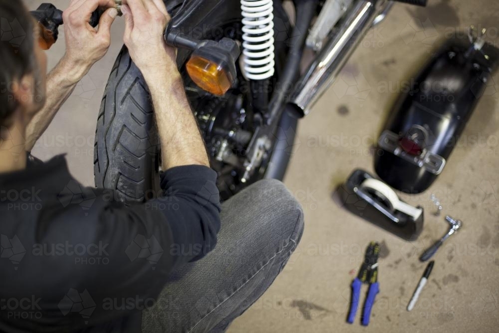 Motorcycle mechanic working on motorbike in garage - Australian Stock Image