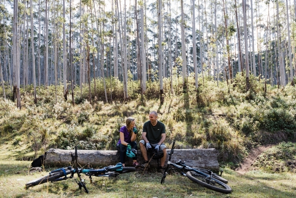 Mountain bike couple rest on a fallen tree - Australian Stock Image