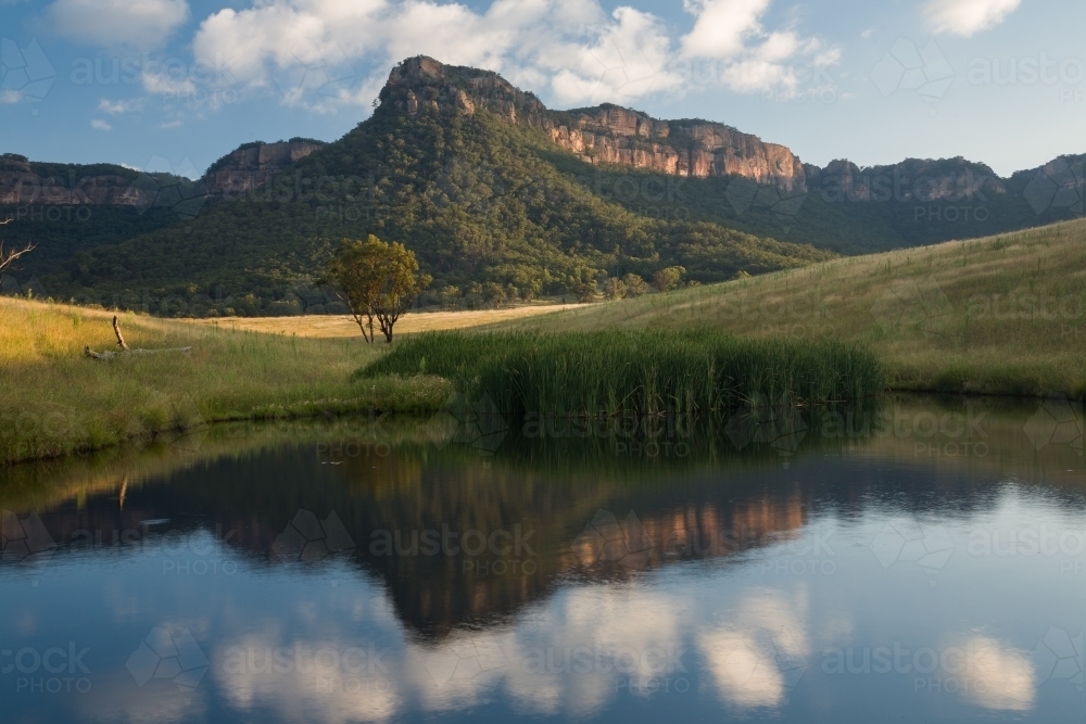 Mountain, paddock and sky reflected in farm dam water - Australian Stock Image