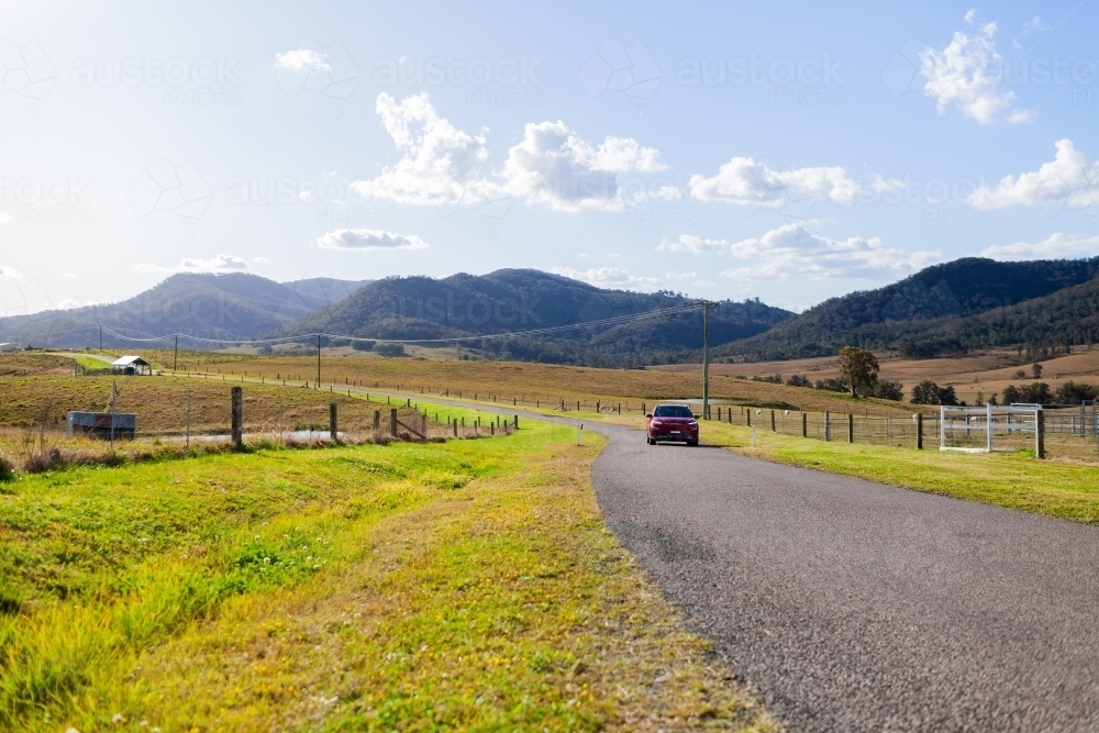 Mountain scenery with country road winding through and red electric car driving - Australian Stock Image