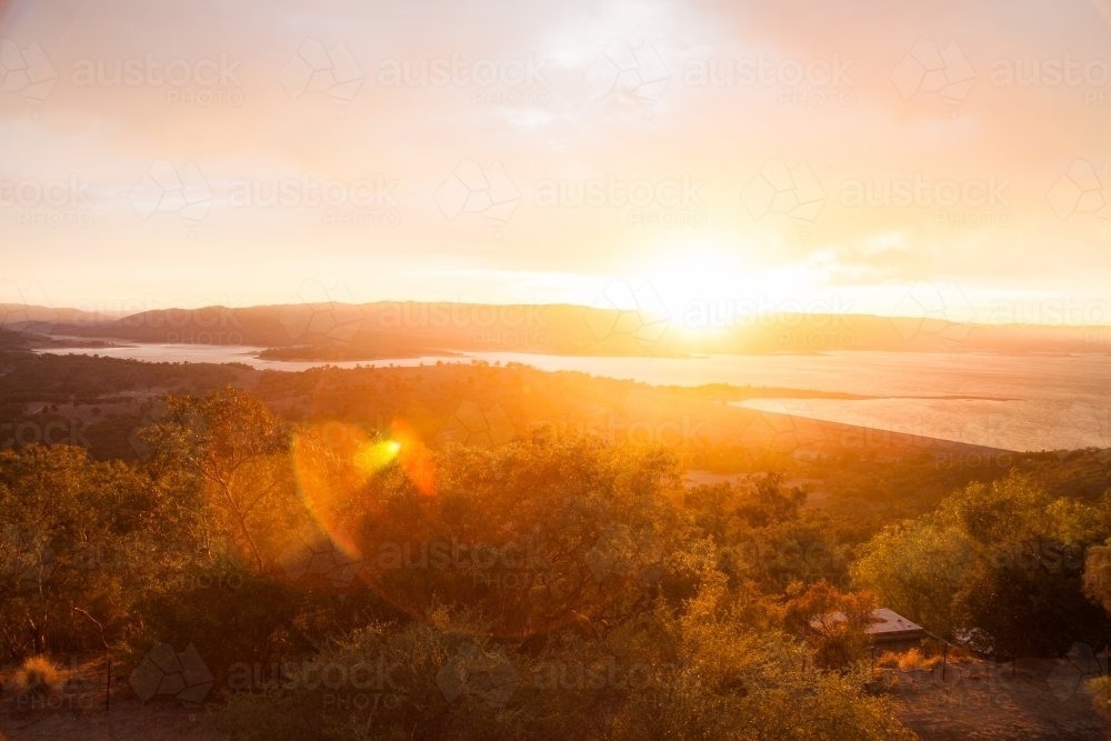 Mountain top lookout over lake with golden sunrise and sun flare - Australian Stock Image