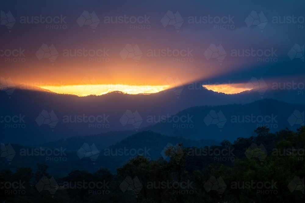 Mountains with sun rays piercing clouds at sunset - Australian Stock Image