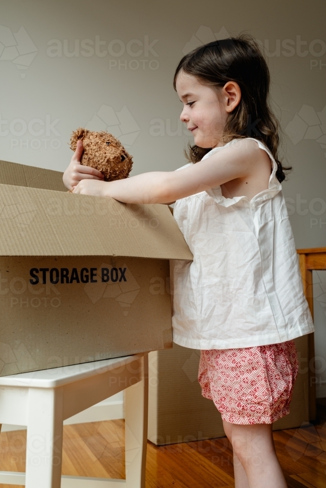 Moving house - Young girl holding her beloved teddy bear inside a cardboard storage box - Australian Stock Image