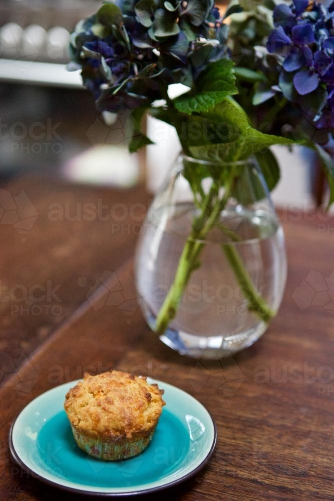 Muffin on an aquamarine plate with a vase of hydrangeas - Australian Stock Image
