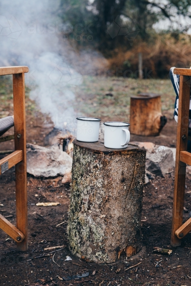 Mugs on tree stump by campfire - Australian Stock Image