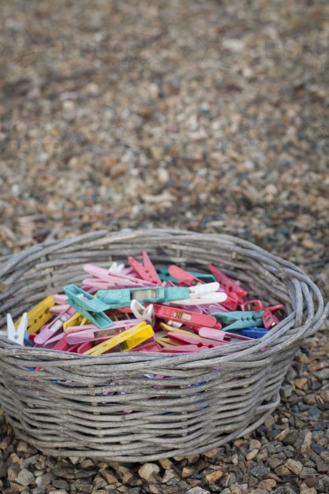 Multi coloured clothes pegs in a wicker basket with a pebble background - Australian Stock Image