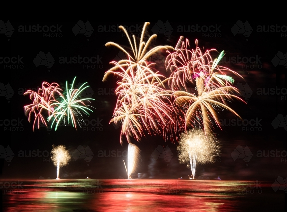 Multi coloured fireworks exploding over an ocean in the night sky. - Australian Stock Image
