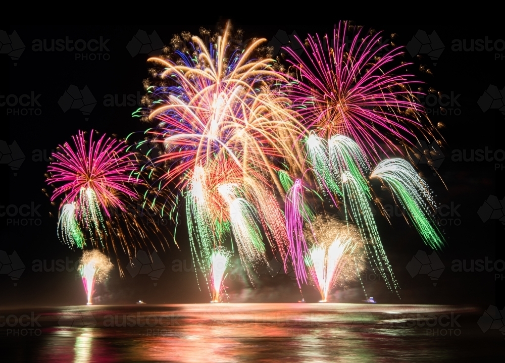 Image of Multi coloured fireworks exploding over an ocean in the night ...