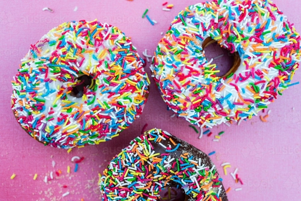 multi coloured sprinkles on donut, on pink background - Australian Stock Image