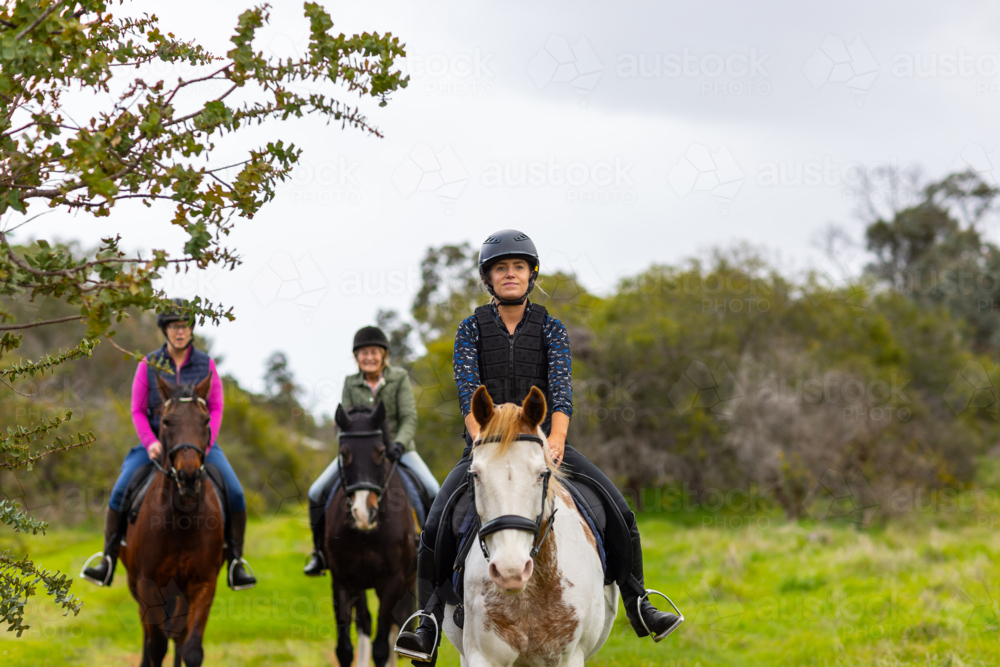 Multi-generation women riding horses along a narrow dirt path. - Australian Stock Image