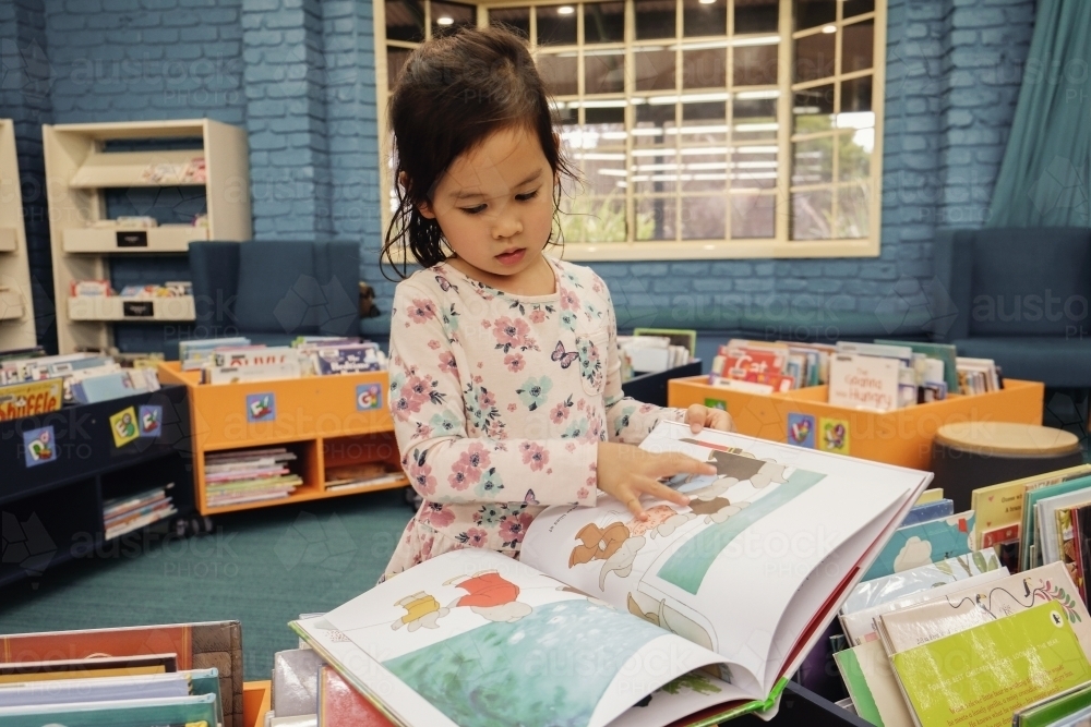 Multicultural child reading a book in library - Australian Stock Image