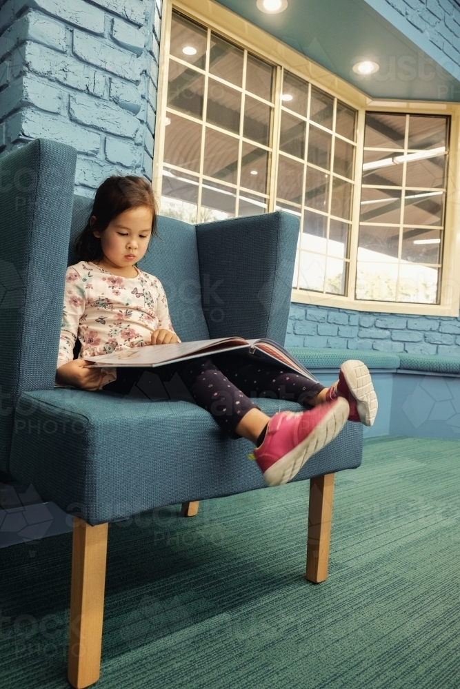 Multicultural child reading a book in library - Australian Stock Image