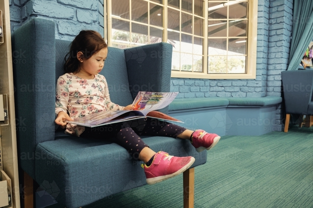 Multicultural girl reading a book in library - Australian Stock Image