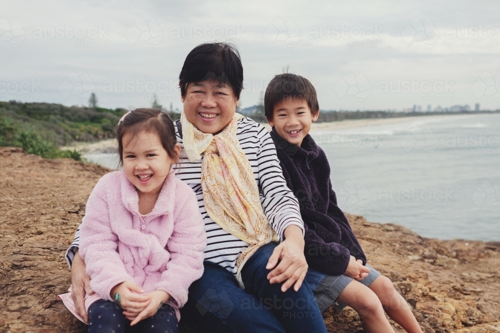 Multicultural grandchildren hug Asian grandmother - Australian Stock Image