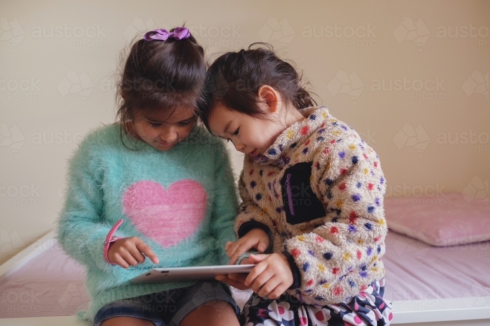 Multicultural kids using tablet in bedroom - Australian Stock Image