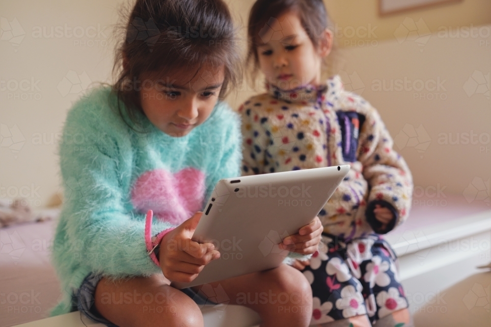 Multicultural kids using tablet in bedroom - Australian Stock Image