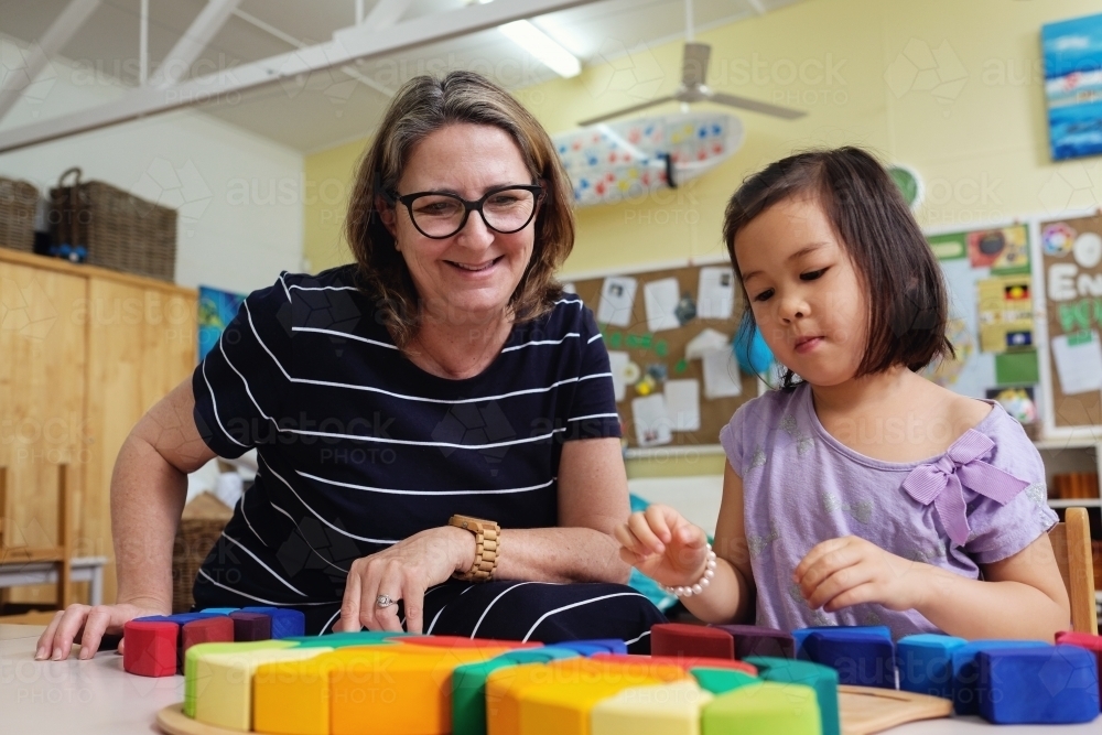 Multicultural teacher and child playing wooden blocks puzzles in kindergarten - Australian Stock Image