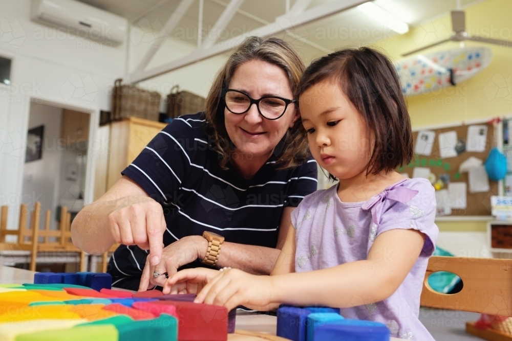 Multicultural teacher and child playing wooden blocks puzzles in kindergarten - Australian Stock Image